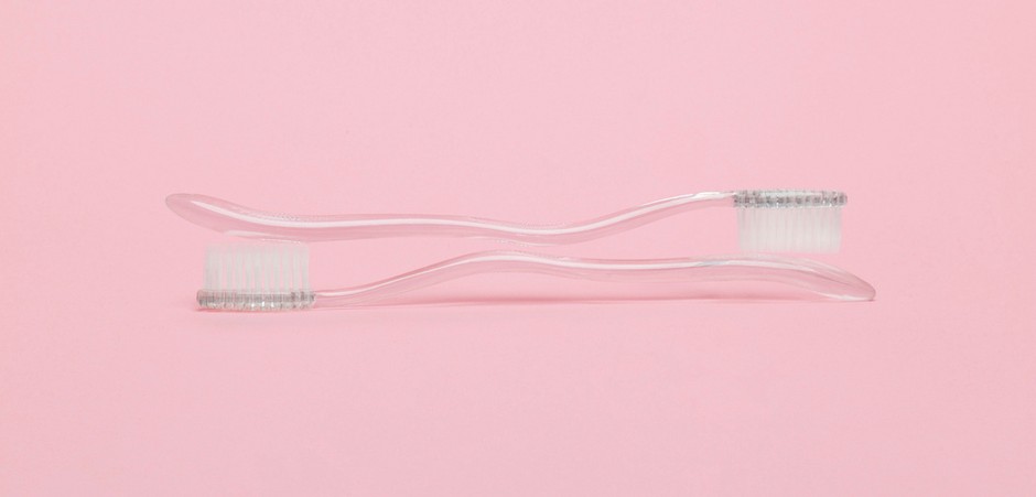A photo of two toothbrushes on top of each other, in front of a light pink background.